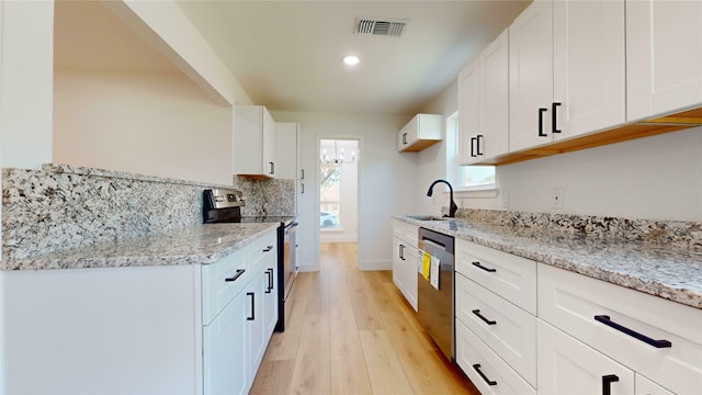 kitchen with sink, white cabinetry, appliances with stainless steel finishes, light stone countertops, and light hardwood / wood-style floors