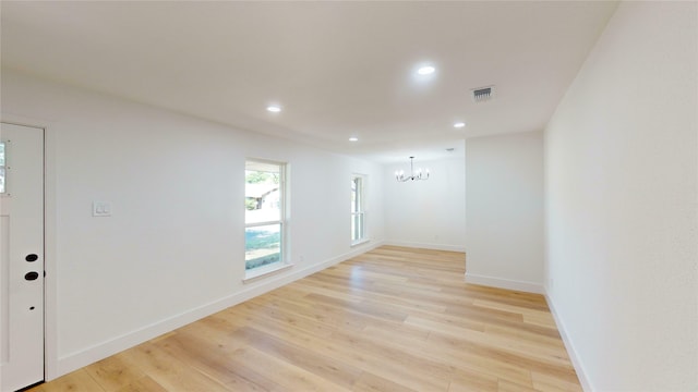 empty room featuring an inviting chandelier and light hardwood / wood-style flooring