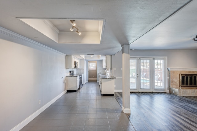 unfurnished living room featuring track lighting, a raised ceiling, crown molding, hardwood / wood-style floors, and a tiled fireplace