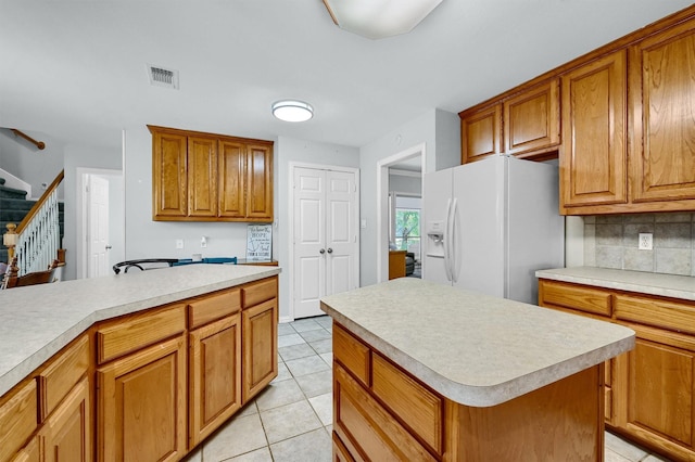 kitchen featuring a center island, white refrigerator with ice dispenser, backsplash, and light tile patterned floors