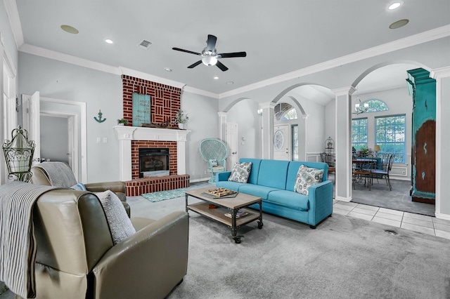 tiled living room with decorative columns, ceiling fan, ornamental molding, and a brick fireplace