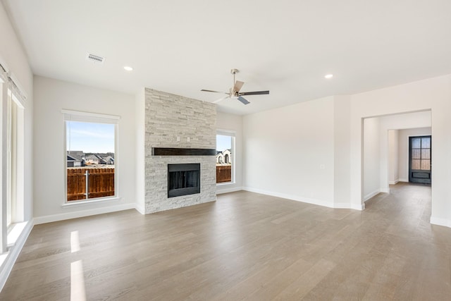 unfurnished living room featuring ceiling fan, a stone fireplace, and light hardwood / wood-style floors