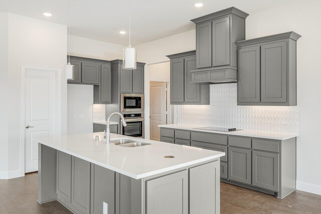 kitchen with built in microwave, sink, gray cabinetry, a kitchen island with sink, and stainless steel oven