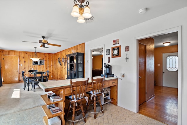 kitchen featuring light wood-type flooring, hanging light fixtures, wood walls, and ceiling fan