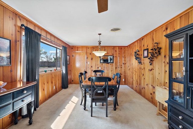 dining area with crown molding, wood walls, and light colored carpet