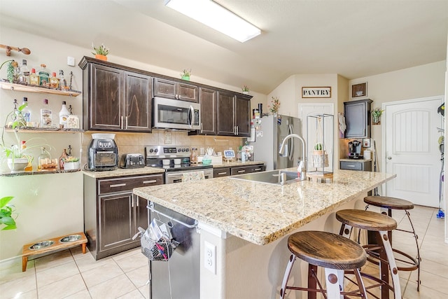 kitchen with decorative backsplash, a breakfast bar, dark brown cabinets, a center island with sink, and stainless steel appliances