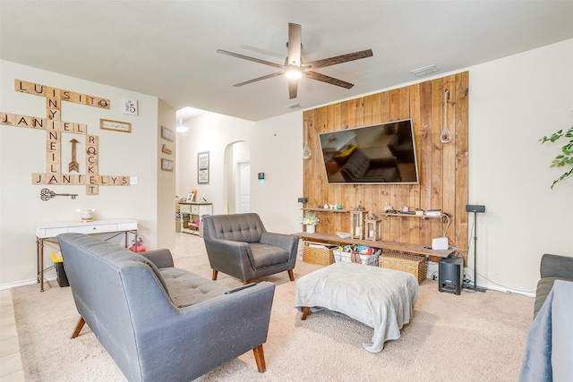 carpeted living room with ceiling fan and wood walls