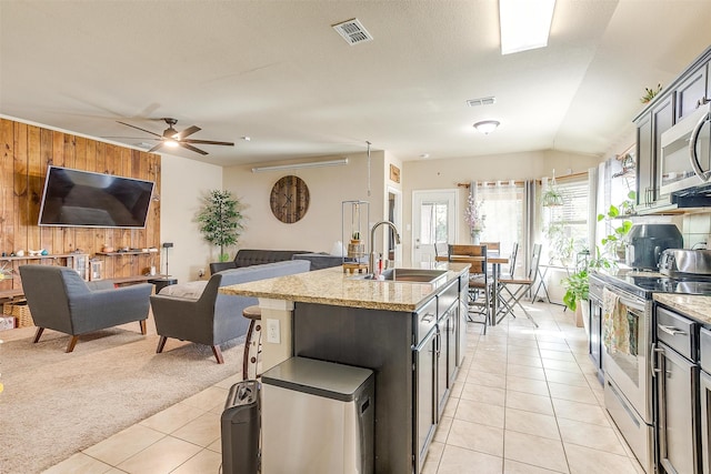 kitchen with sink, a center island with sink, stainless steel appliances, light carpet, and light stone countertops