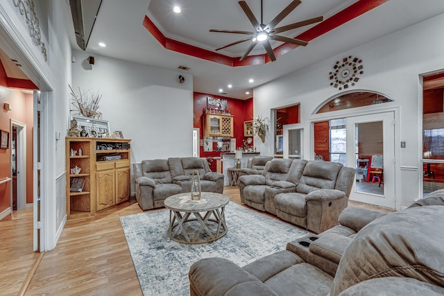 living room with light wood-type flooring, crown molding, a high ceiling, and ceiling fan