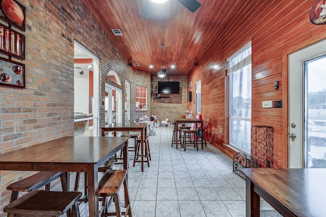 dining area featuring ceiling fan, light tile patterned flooring, wood ceiling, wood walls, and brick wall