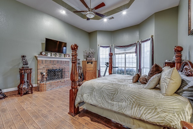 bedroom featuring a brick fireplace, light hardwood / wood-style floors, and ceiling fan