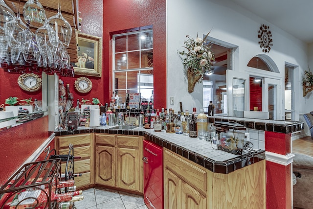 kitchen with kitchen peninsula, sink, light tile patterned floors, and tile countertops