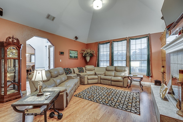 living room with light hardwood / wood-style flooring, a tile fireplace, and high vaulted ceiling