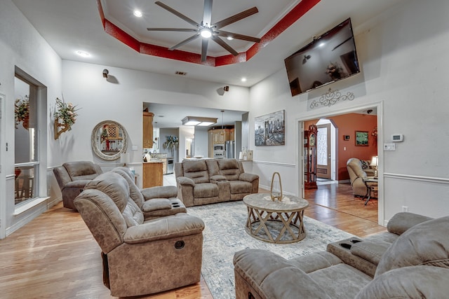 living room featuring a towering ceiling, light wood-type flooring, a tray ceiling, ceiling fan, and ornamental molding