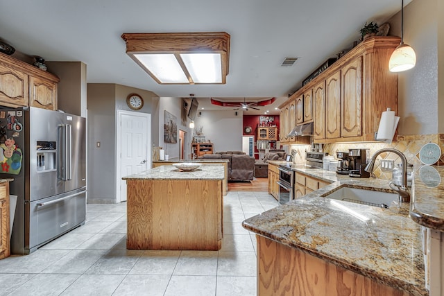 kitchen with light stone counters, stainless steel appliances, a center island, ceiling fan, and sink