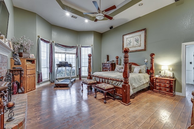 bedroom with ceiling fan, a fireplace, a towering ceiling, and light hardwood / wood-style floors