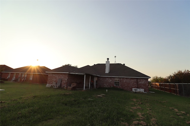 back house at dusk featuring a lawn