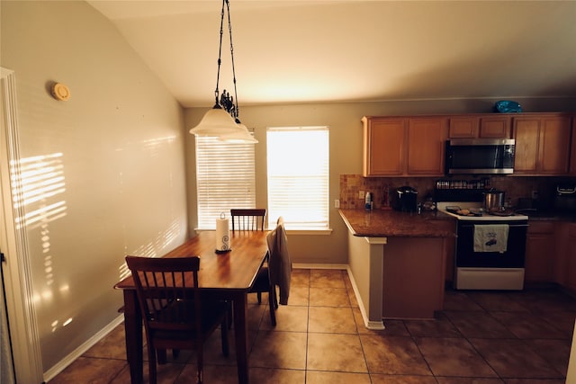 kitchen with dark tile patterned flooring, lofted ceiling, hanging light fixtures, tasteful backsplash, and white range with electric stovetop