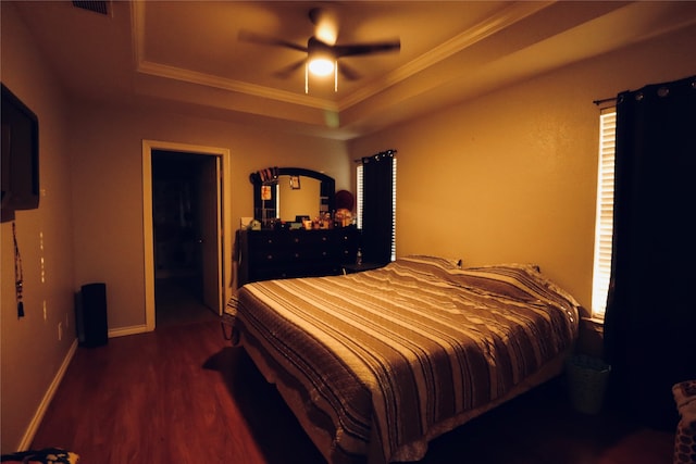 bedroom with ceiling fan, ornamental molding, a raised ceiling, and dark wood-type flooring