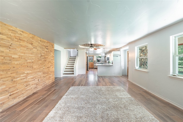 unfurnished living room with wood walls, ceiling fan, and hardwood / wood-style flooring