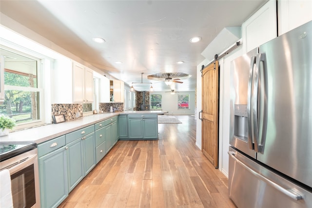 kitchen featuring white cabinets, kitchen peninsula, stainless steel appliances, light wood-type flooring, and a barn door