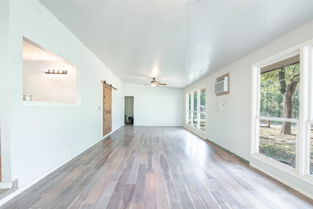 unfurnished living room with a barn door, wood-type flooring, an AC wall unit, and a wealth of natural light