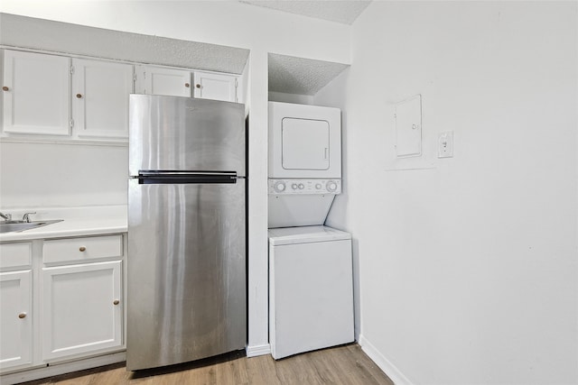 interior space with light wood-type flooring, a textured ceiling, white cabinetry, stainless steel fridge, and stacked washer and clothes dryer