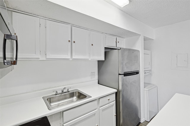 kitchen featuring white cabinetry, stainless steel refrigerator, a textured ceiling, stacked washer and dryer, and sink