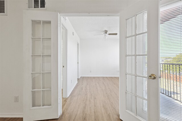 hall with a textured ceiling, light hardwood / wood-style floors, and french doors