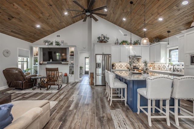 kitchen with appliances with stainless steel finishes, a kitchen breakfast bar, dark wood-type flooring, light stone countertops, and decorative light fixtures