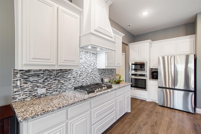 kitchen featuring dark hardwood / wood-style flooring, custom range hood, backsplash, appliances with stainless steel finishes, and white cabinetry