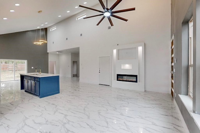 kitchen featuring a center island with sink, sink, blue cabinetry, high vaulted ceiling, and decorative light fixtures