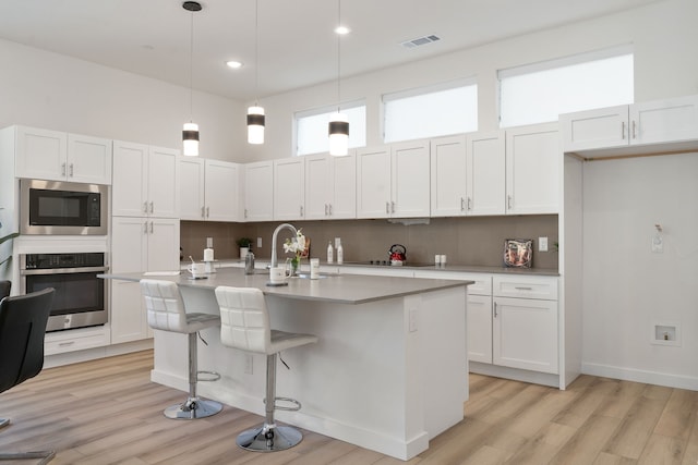 kitchen featuring appliances with stainless steel finishes, white cabinetry, pendant lighting, and an island with sink