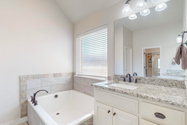 bathroom featuring vanity, a relaxing tiled tub, and vaulted ceiling