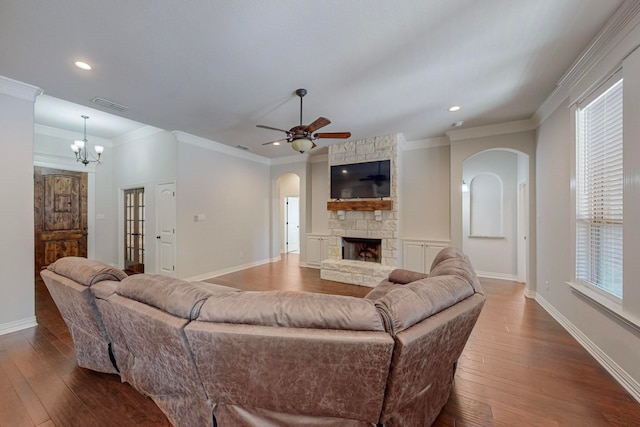 living room featuring a stone fireplace, hardwood / wood-style flooring, ceiling fan with notable chandelier, and ornamental molding