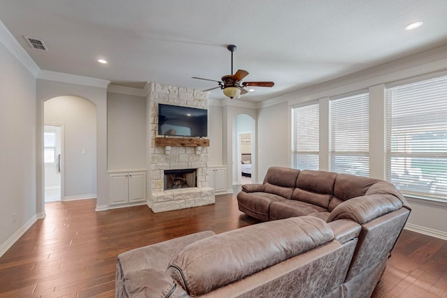 living room featuring a stone fireplace, ornamental molding, dark hardwood / wood-style flooring, and ceiling fan