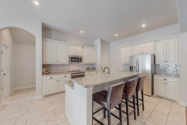 kitchen featuring decorative backsplash, white cabinetry, an island with sink, light stone counters, and stainless steel appliances