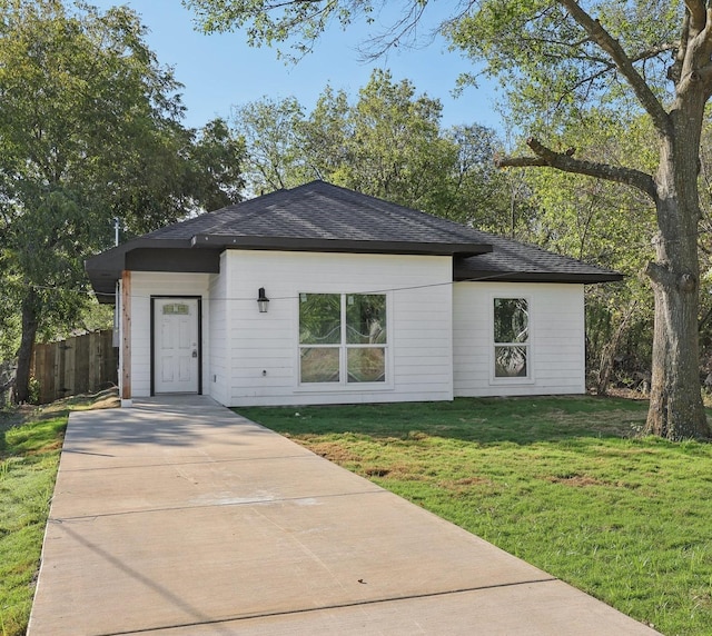 view of front of house with a shingled roof, fence, and a front yard