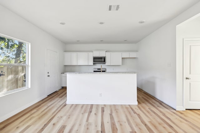 kitchen with visible vents, white cabinets, stainless steel microwave, light countertops, and light wood-type flooring