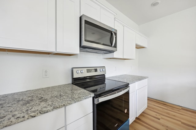 kitchen featuring appliances with stainless steel finishes, white cabinetry, light wood finished floors, and light stone counters