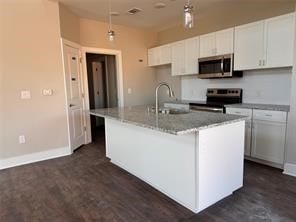 kitchen featuring light stone counters, a kitchen island with sink, sink, white cabinets, and appliances with stainless steel finishes