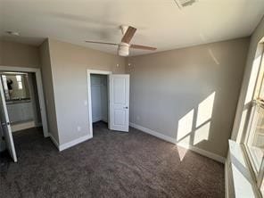 unfurnished bedroom with dark carpet, a closet, a spacious closet, and ceiling fan