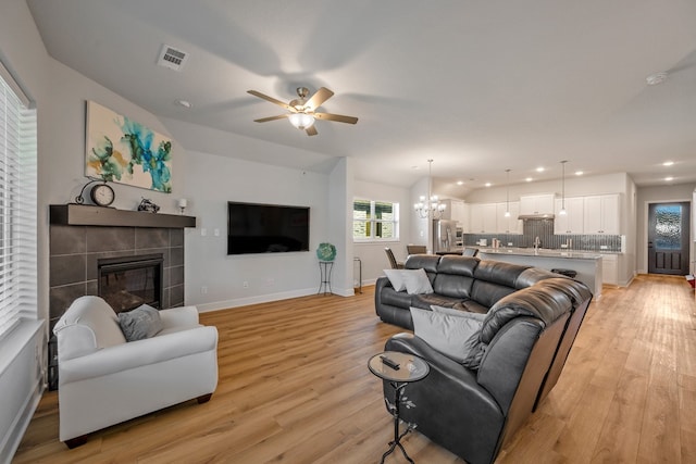 living room featuring ceiling fan with notable chandelier, light hardwood / wood-style flooring, and a tiled fireplace