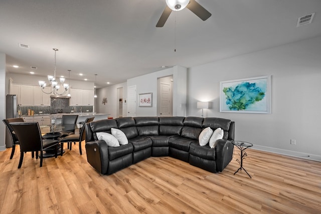 living room with ceiling fan with notable chandelier and light hardwood / wood-style flooring