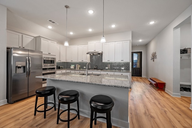 kitchen featuring white cabinets, stainless steel appliances, light wood-type flooring, and tasteful backsplash