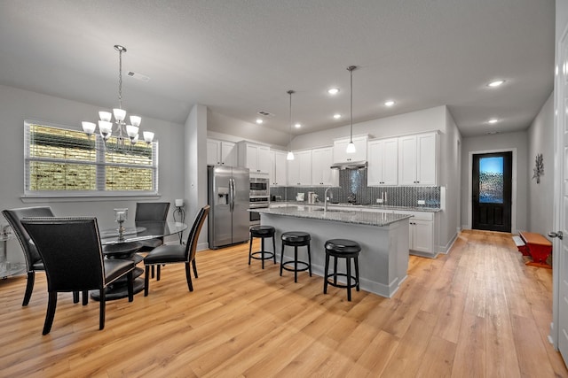 kitchen with white cabinets, hanging light fixtures, a center island with sink, light hardwood / wood-style flooring, and stainless steel appliances