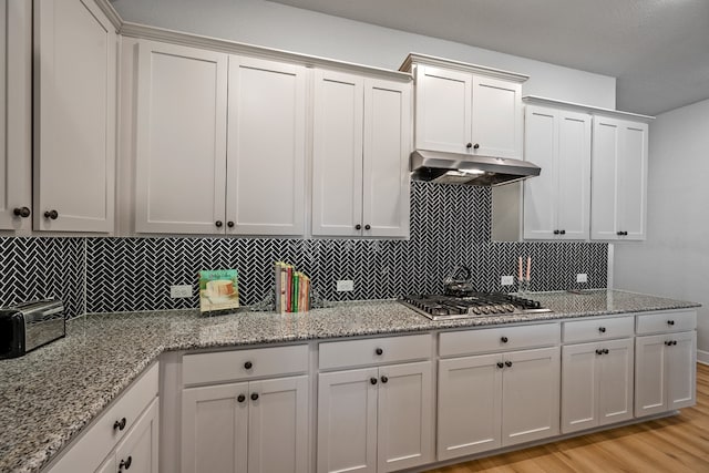 kitchen with light wood-type flooring, white cabinets, stainless steel gas cooktop, and backsplash