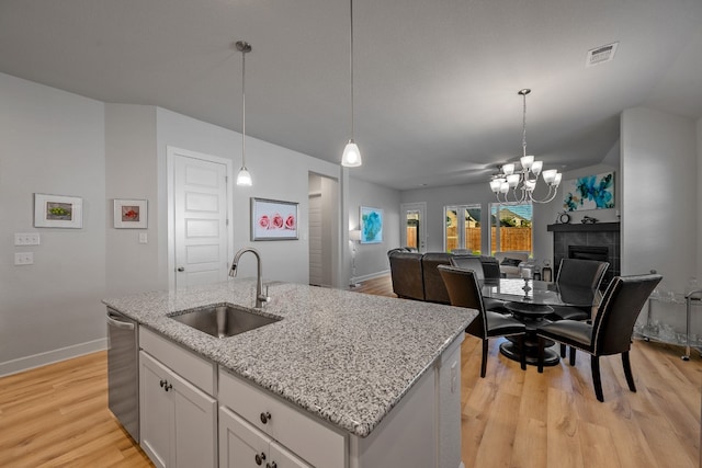 kitchen with white cabinets, sink, a kitchen island with sink, light hardwood / wood-style flooring, and a tiled fireplace