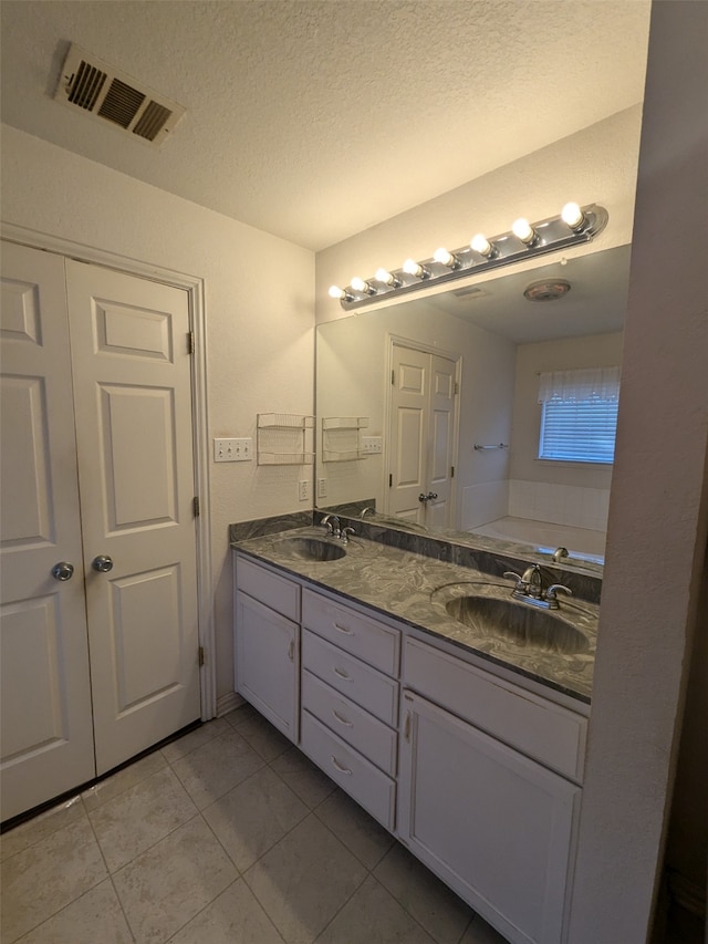 bathroom with vanity, a textured ceiling, a washtub, and tile patterned flooring