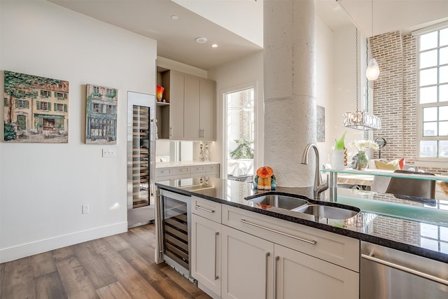 kitchen featuring dark stone counters, hardwood / wood-style flooring, sink, beverage cooler, and hanging light fixtures